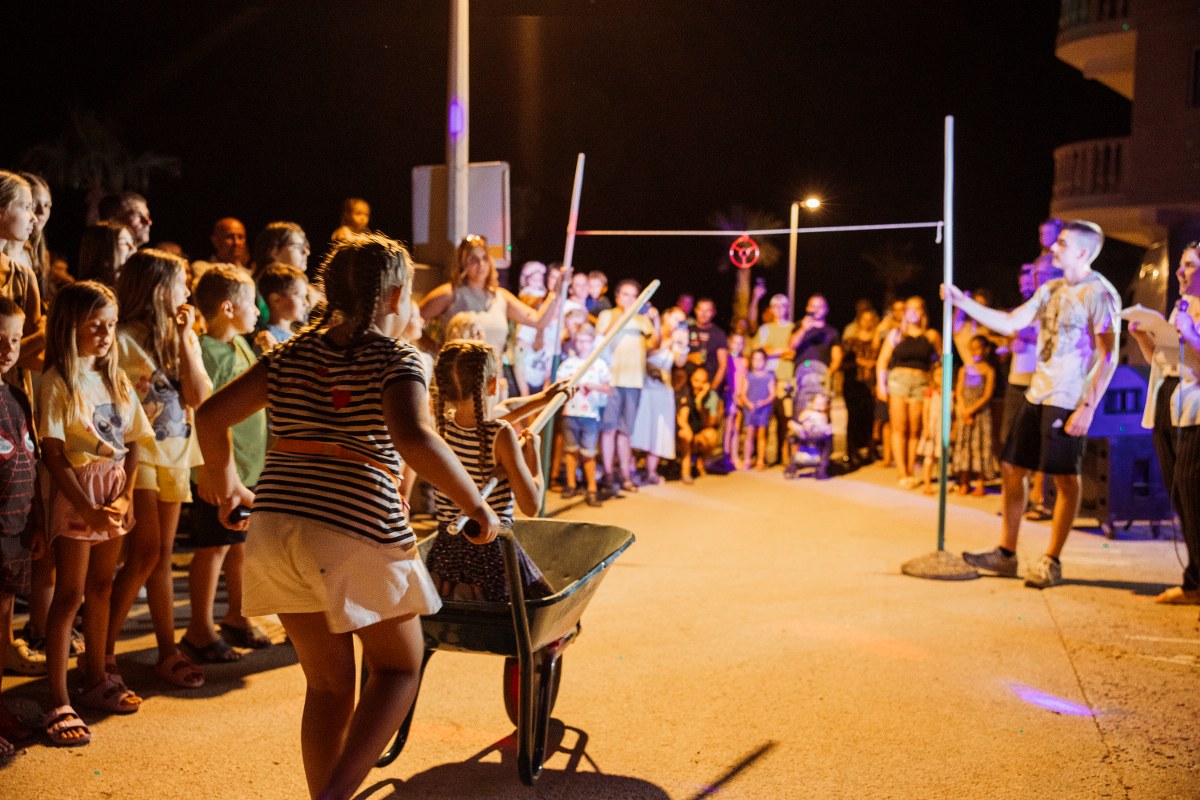 Children playing a ring-tilting game called alka with a wheelbarrow at a night event in Drašnice