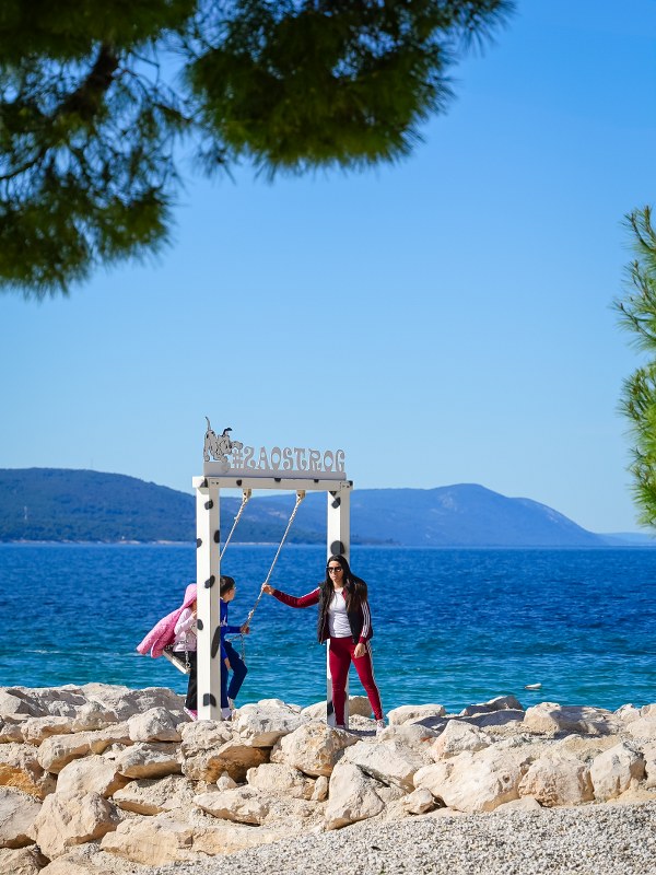 People on a wooden swing frame by the sea in Zaostrog