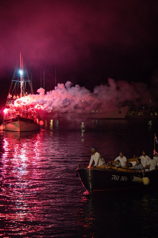 Fireworks and red smoke over the water with a boat at night
