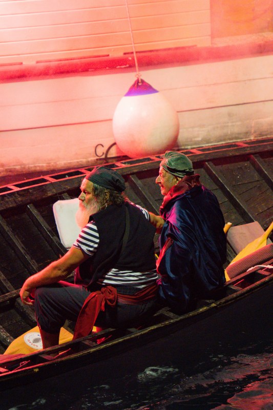 Two men in costume rowing a boat lit in red smoke