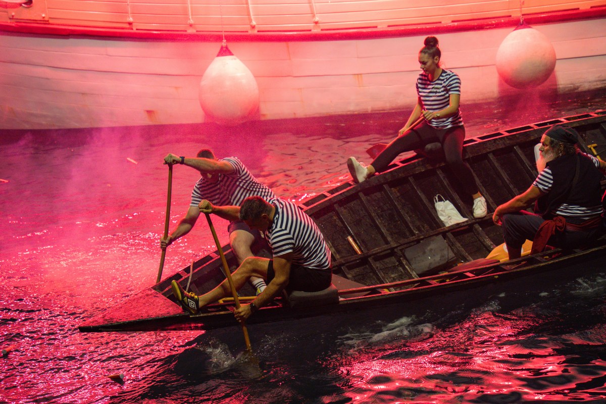 Man in costume rowing a boat surrounded by pink smoke
